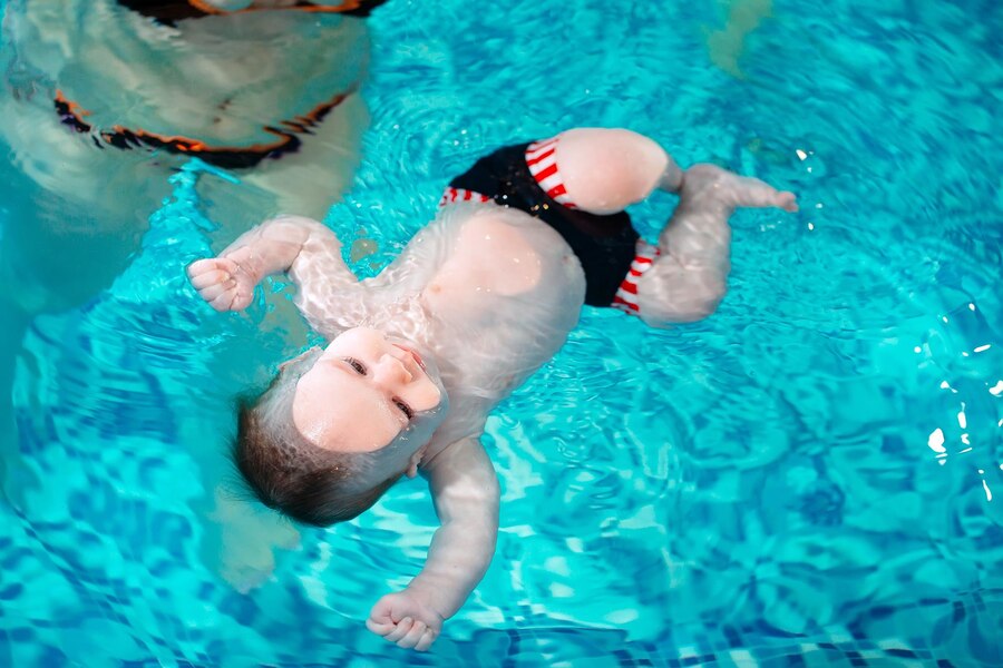 Bebé flotando en el agua de la piscina mientras realiza natación.