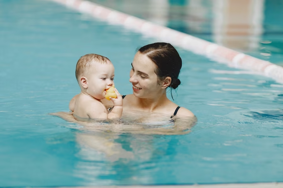 Bebé con su madre practicando natación dentro de una piscina.